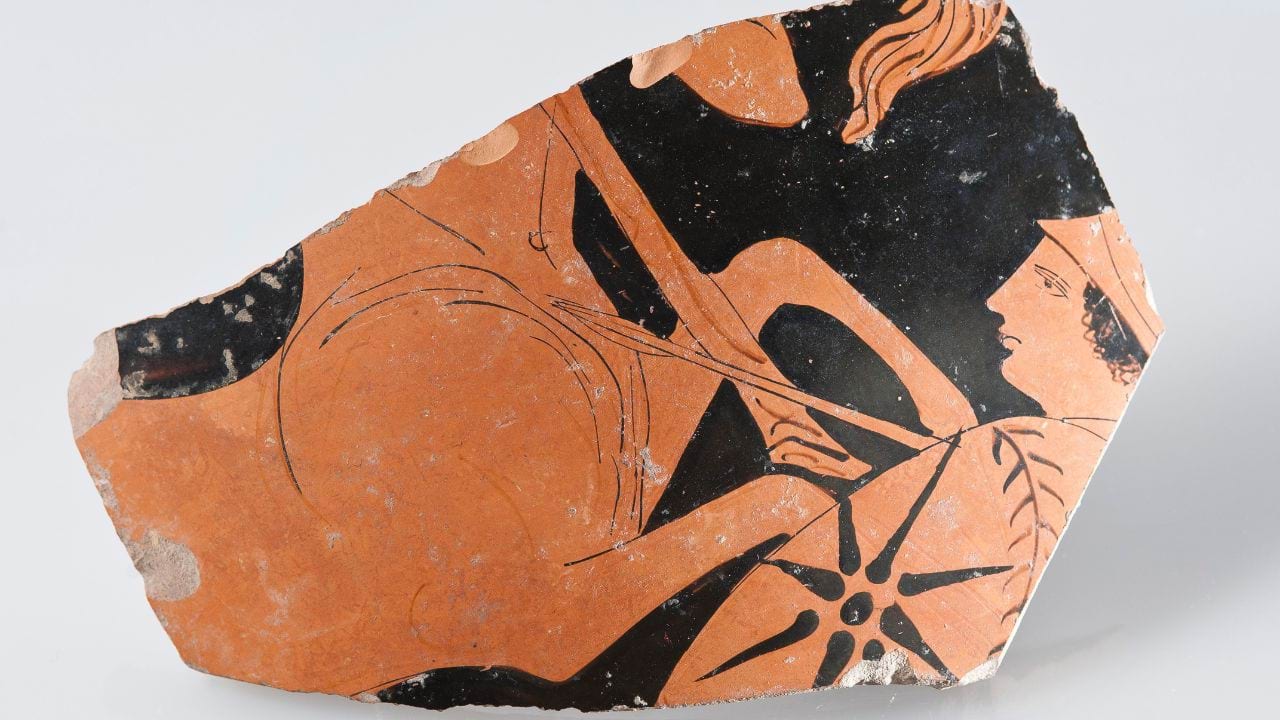 Close up of a fragment of a vase with paintings in terracotta and black.