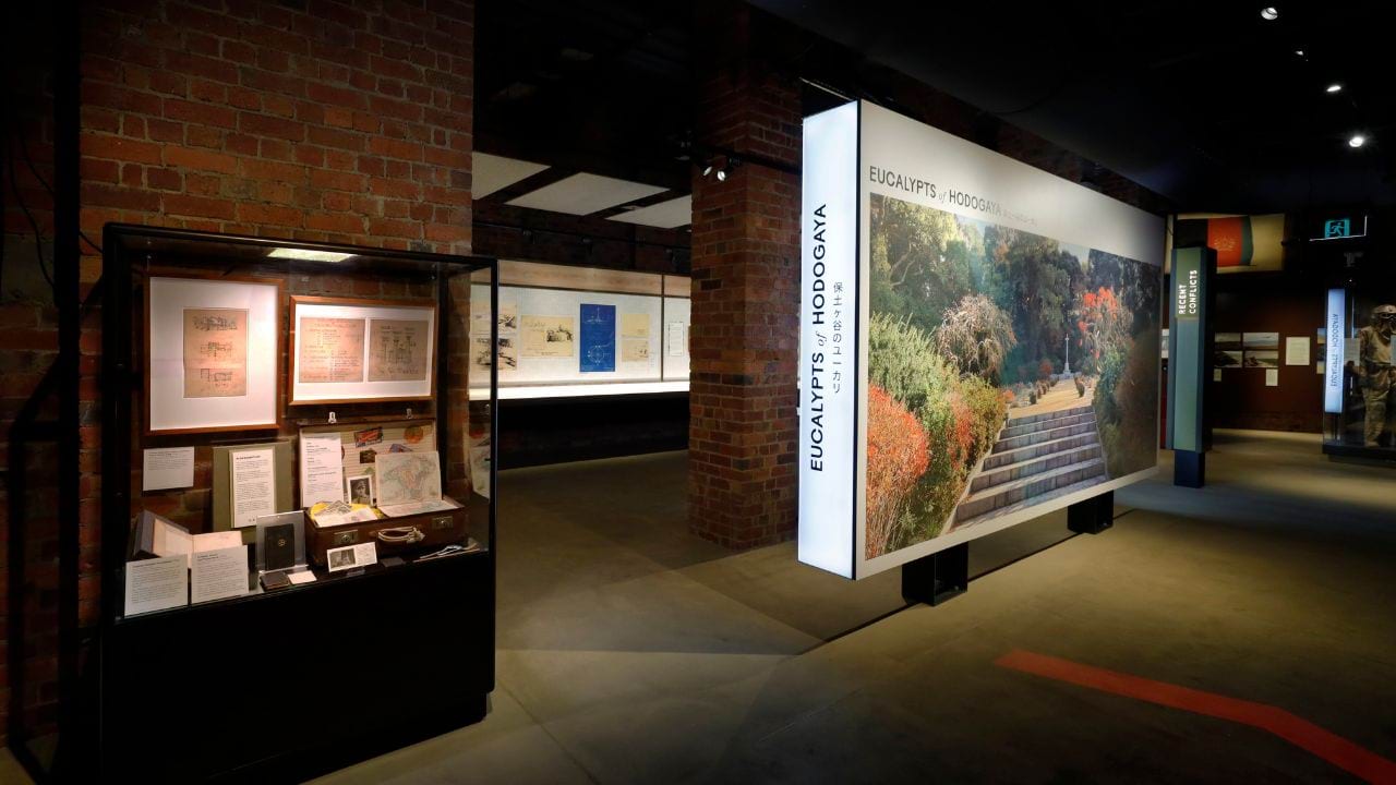 Dimly lit exhibition space showcasing the title wall and an exhibition case containing objects and artefacts.